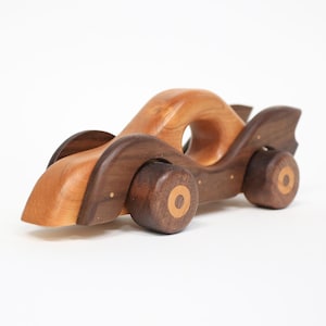 以下が含まれることがあります： 流線型のデザインの木製おもちゃの車。車は明るい茶色のボディと濃い茶色のシャーシ、ホイール、アクセントを備えています。ホイールの中央には明るい茶色の円があります。子供向けのユニークな木製おもちゃ。