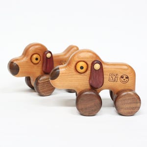 Op de afbeelding: Twee houten speelgoedhonden met bruine, rode en gele details. De honden hebben wielen en zijn gemaakt van kersenhout. De honden hebben een vrolijk gezicht en een Koreaanse inscriptie aan de zijkant.