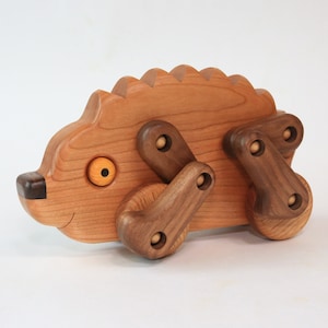 May include: A wooden toy hedgehog with a brown body, a light brown face, and a yellow eye. The hedgehog has four wooden wheels and a brown tail.