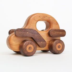 以下が含まれることがあります： 自然な仕上がりと濃い茶色のアクセントが施された木製のおもちゃの車。 車にはハンドル、4つの車輪、シンプルでクラシックなデザインが施されています。 車輪の直径は約7.6cmです。