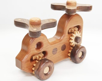 May include: A wooden toy helicopter with brown and natural wood tones. The helicopter has two sets of spinning gears and two propellers. The toy is made of wood and has a natural finish.