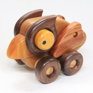 May include: A wooden toy bird with brown, yellow, and black details. The bird has large, round eyes and a beak. It has four wheels made of dark wood.