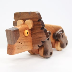 May include: A wooden toy lion with a brown and tan finish. The lion has a large mane, a smiling face, and wheels on its feet.