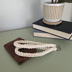 May include: A brown leather wallet with a woven pattern and a white cotton rope handle with silver key rings.