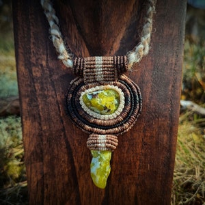Peut inclure: Un collier avec un pendentif en pierre précieuse verte et blanche sur un cordon en macramé brun et blanc. Le pendentif est de forme ronde avec une petite pierre précieuse pointue suspendue en bas.