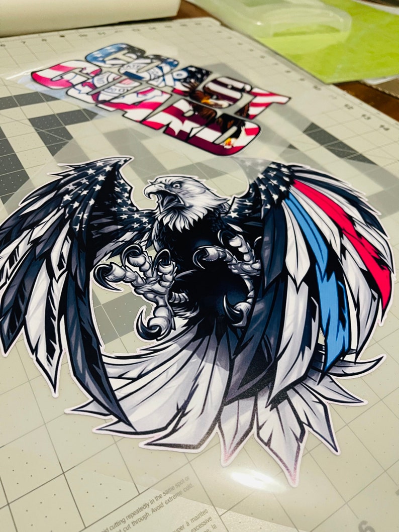 Peut inclure: Un aigle chauve noir et blanc avec ses ailes d&eacute;ploy&eacute;es. L'aigle tient un petit drapeau am&eacute;ricain dans ses serres. Les ailes de l'aigle sont d&eacute;cor&eacute;es des couleurs du drapeau am&eacute;ricain, rouge, blanc et bleu.