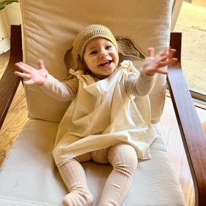 May include: A baby wearing a crocheted Yoda costume, sitting in a chair and smiling.