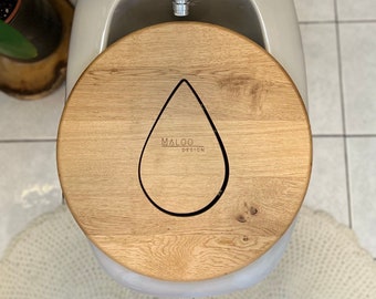 May include: A wooden toilet seat with a teardrop-shaped cutout and the text "MALOO DESIGN" engraved on the top.