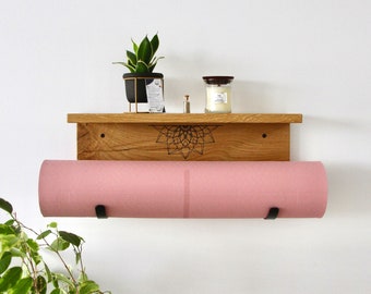 May include: A wooden shelf with a black mandala design and two black metal hooks for hanging a pink yoga mat. A small potted plant and a candle are on the shelf.