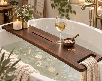 May include: A rectangular dark brown wooden bathtub tray resting across a white bathtub. The tray features a long narrow slot, a glass of white wine, a small wooden bowl with bath salts and a wooden spoon, and a lit candle in a glass jar.