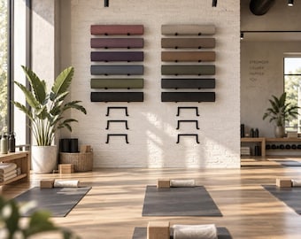 May include: Two vertical wall-mounted racks holding multiple rolled yoga mats in various colours including pink, purple, blue, green, beige, and black. The racks are installed on a white brick wall above black yoga mats on a wooden floor.