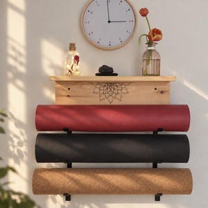 May include: A wall-mounted wooden shelf with a black mandala design, holding three rolled yoga mats in red, black, and cork textures. Above the shelf sits a round wall clock, a clear glass bottle with fairy lights, and a glass vase with orange tulips.