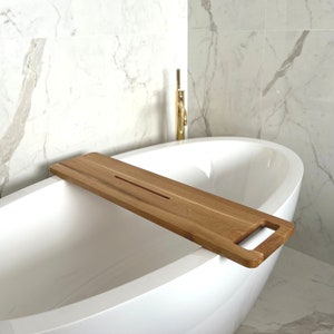 Könnte beinhalten: Ein Holz-Badetablett mit einem Griff und einer Rille zum Halten von Gegenständen. Das Tablett liegt am Rand einer weißen Badewanne.