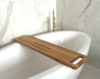 May include: A wooden bath tray with a handle and a groove for holding items. The tray is placed on the edge of a white bathtub.