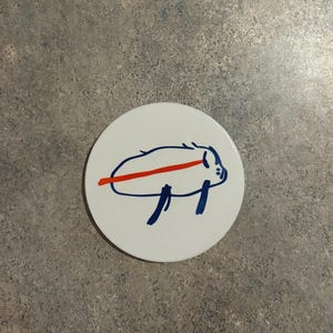 May include: White ceramic coaster with a blue and red hand-drawn illustration of a pig.