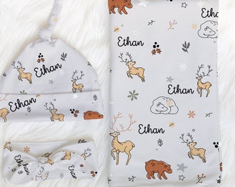 May include: A baby gift set featuring a grey and white hat, headband, and blanket. The hat and headband have a deer and bear print with the name "Ethan" repeated on each item. The blanket has a similar print with the name "Ethan" repeated.