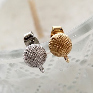 May include: Two small round earring findings, one gold and one silver, with a textured surface and a small loop at the bottom.