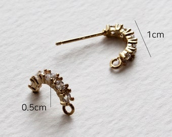 May include: A pair of gold-toned earring findings with a curved shape and a row of clear rhinestones. The findings are 1 cm long and 0.5 cm wide.