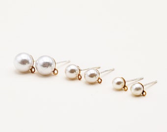 May include: A collection of pearl stud earrings in varying sizes. The earrings have a classic design with a white, round pearl attached to a silver post with a gold-colored loop.
