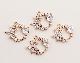 May include: Four gold-colored charms with a floral and heart design. Each charm features a flower made of clear crystals, a heart-shaped crystal, and a ring of smaller crystals. The charms have a loop at the top for attaching to jewelry.