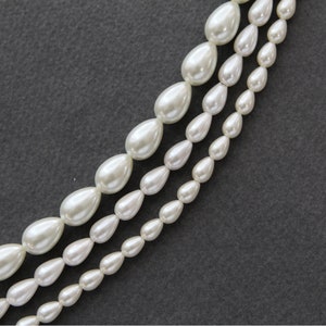 May include: A strand of white pearl beads, with each pearl shaped like a teardrop. The pearls are arranged in three rows, with the largest pearls in the centre row and the smallest pearls on the outer rows.