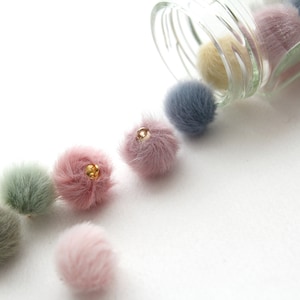 May include: A glass jar filled with colorful fuzzy pom poms. The pom poms are spilling out of the jar and are in shades of pink, blue, and yellow.
