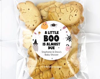 May include: A clear cellophane bag filled with Halloween-themed cookies. The cookies are light brown and shaped like ghosts and other festive shapes. A round sticker on the bag reads "A Little Boo Is Almost Due" and is for Stephanie & Drew's Baby Shower.