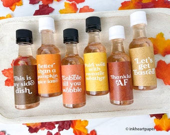 May include: Six small glass bottles with colorful labels and autumn-themed sayings. The labels include "This is my side dish", "Better than a pumpkin spice latte", "Gobble till you wobble", "Pairs well with sweater weather", "Thankful AF", and "Let's get basted".