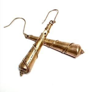 Pode incluir: Um par de brincos dourados com um design em espiral. Os brincos têm uma forma cilíndrica com um detalhe de fio enrolado e um pequeno elemento decorativo na parte inferior. Os ganchos são prateados.