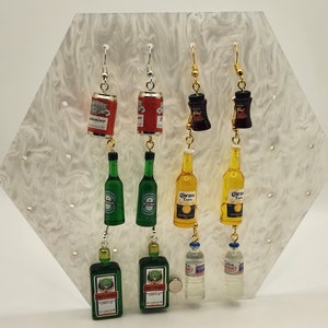 May include: A set of dangle earrings featuring miniature replicas of popular alcoholic beverages. The earrings include a green beer bottle, a yellow beer bottle, a red can, a black bottle, and a clear water bottle.