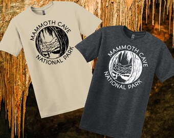 May include: Two short-sleeved t-shirts, one beige and one charcoal grey, with a circular graphic reading "Mammoth Cave National Park." The graphic shows a cave entrance. The shirts are casual wear.