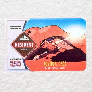 May include: A Resident Annual pass for Joshua Tree National Park. The pass features a desert landscape illustration with a bright sun and the park's name in orange. The pass also includes the America 250 logo.