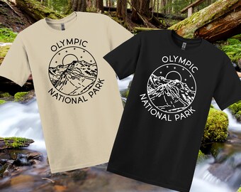 May include: Two t-shirts, one beige and one black, each with a circular graphic. The graphic features a mountain range, sun, and stars, with the text "OLYMPIC NATIONAL PARK" in a circle. The shirts are short-sleeved.