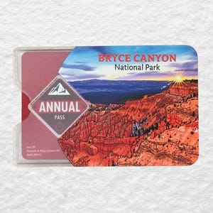 May include: A rectangular annual pass for Bryce Canyon National Park. The pass is in a clear plastic holder. The pass features a landscape illustration of the park with the text "Bryce Canyon National Park" and "Annual Pass".
