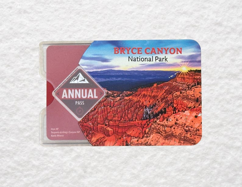 May include: A rectangular annual pass for Bryce Canyon National Park. The pass is in a clear plastic holder. The pass features a landscape illustration of the park with the text "Bryce Canyon National Park" and "Annual Pass".