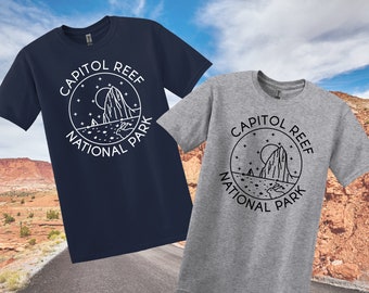May include: Two t-shirts featuring a graphic design of a mountain range and the text "Capitol Reef National Park". The t-shirt on the left is navy blue and the t-shirt on the right is grey.