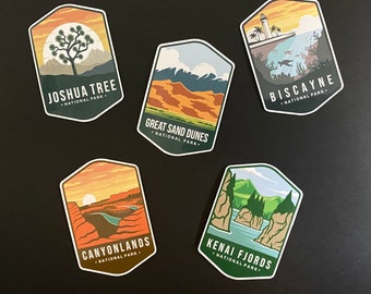 May include: Five colourful stickers featuring different national parks in the United States. Each sticker has a unique design with a landscape scene and the park's name and "National Park" written below. The stickers are on a black background.