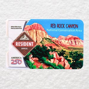 May include: A Resident Annual pass for Red Rock Canyon National Conservation Area. The pass features a scenic illustration of the canyon with red rock formations and green vegetation. The pass also includes the text "America 250".