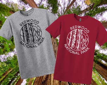May include: Two short-sleeved t-shirts, one grey and one red, with a circular graphic reading "REDWOOD NATIONAL PARK." The design shows trees, a mountain range, and a crescent moon.