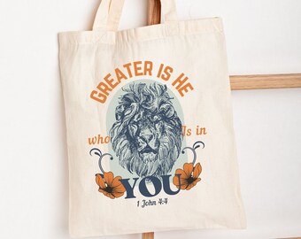 May include: A beige tote bag with a lion graphic and the text "GREATER IS HE who is in YOU 1 John 4:4".