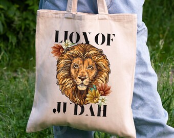 May include: A beige canvas tote bag with the text "Lion of Judah" in black lettering. A lion's head with a mane is depicted in the center of the bag, surrounded by colorful flowers.