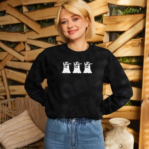 May include: Black sweatshirt with a white graphic of three ghosts wearing hats and holding their arms out. The ghosts are smiling.