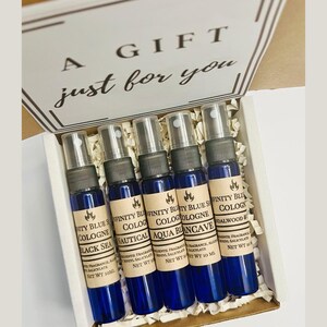 May include: A gift box containing five small blue bottles with brown labels. The labels read "Infinity Blue Cologne" with different scents: "Black Sea", "Nautical", "Aqua", "Blancave", and "Sandalwood & Cedar". The box is white with the words "A Gift just for you" printed on the top.