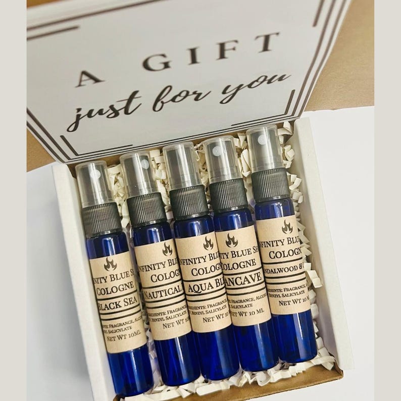 May include: A gift box containing five small blue bottles with brown labels. The labels read "Infinity Blue Cologne" with different scents: "Black Sea", "Nautical", "Aqua", "Blancave", and "Sandalwood & Cedar". The box is white with the words "A Gift just for you" printed on the top.