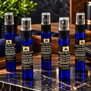 May include: Five cylindrical blue glass spray bottles of Infinity Blue Shop cologne, each with a black spray nozzle and a label reading Infinity Blue Shop Cologne, listing ingredients and a net weight of 10 ml, arranged in a row.