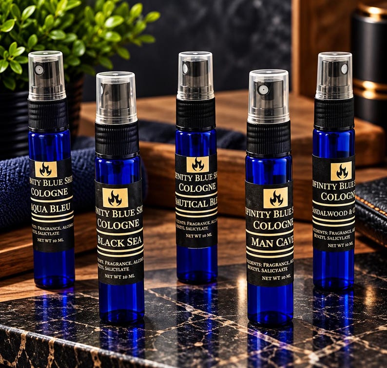 May include: Five cylindrical blue glass spray bottles of Infinity Blue Shop cologne, each with a black spray nozzle and a label reading Infinity Blue Shop Cologne, listing ingredients and a net weight of 10 ml, arranged in a row.