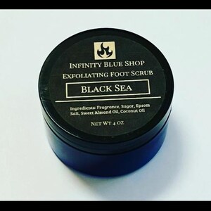 May include: A round black container of Infinity Blue Shop Exfoliating Foot Scrub in the Black Sea scent. The black label features a flame icon, the product name, and a list of ingredients including fragrance, sugar, Epsom salt, and oils. Net wt 4 oz.