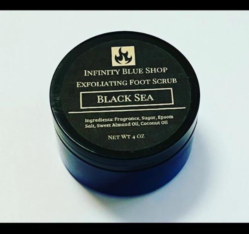 May include: A round black container of Infinity Blue Shop Exfoliating Foot Scrub in the Black Sea scent. The black label features a flame icon, the product name, and a list of ingredients including fragrance, sugar, Epsom salt, and oils. Net wt 4 oz.