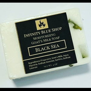 May include: A rectangular bar of white goat's milk soap with green botanical inclusions. A black label features the text Infinity Blue Shop, Moisturizing Goat's Milk Soap, Black Sea, and a list of ingredients with a net weight of 4 oz.