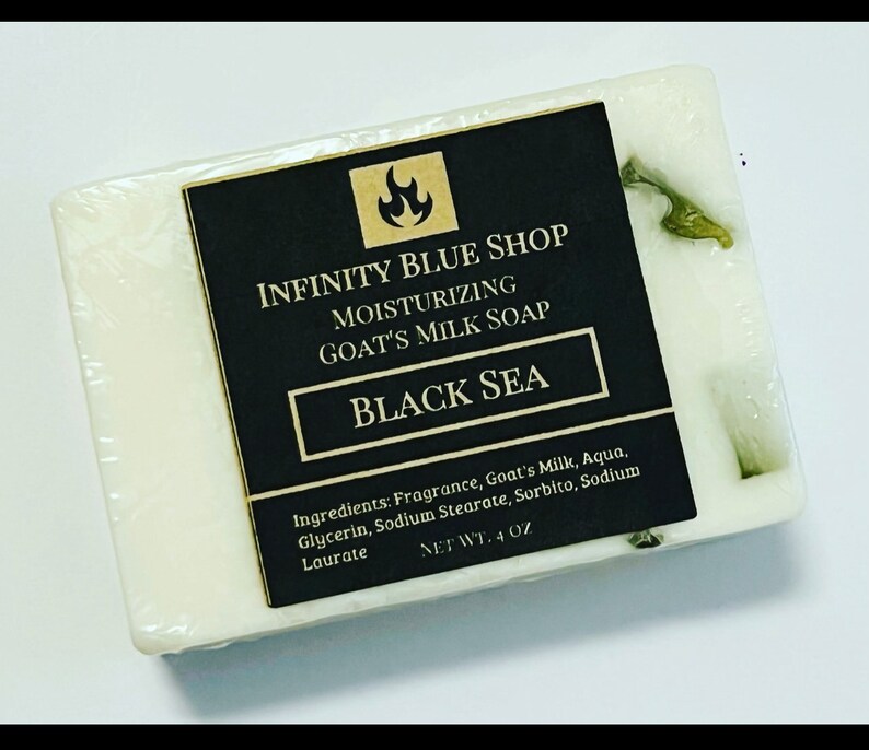 May include: A rectangular bar of white goat's milk soap with green botanical inclusions. A black label features the text Infinity Blue Shop, Moisturizing Goat's Milk Soap, Black Sea, and a list of ingredients with a net weight of 4 oz.